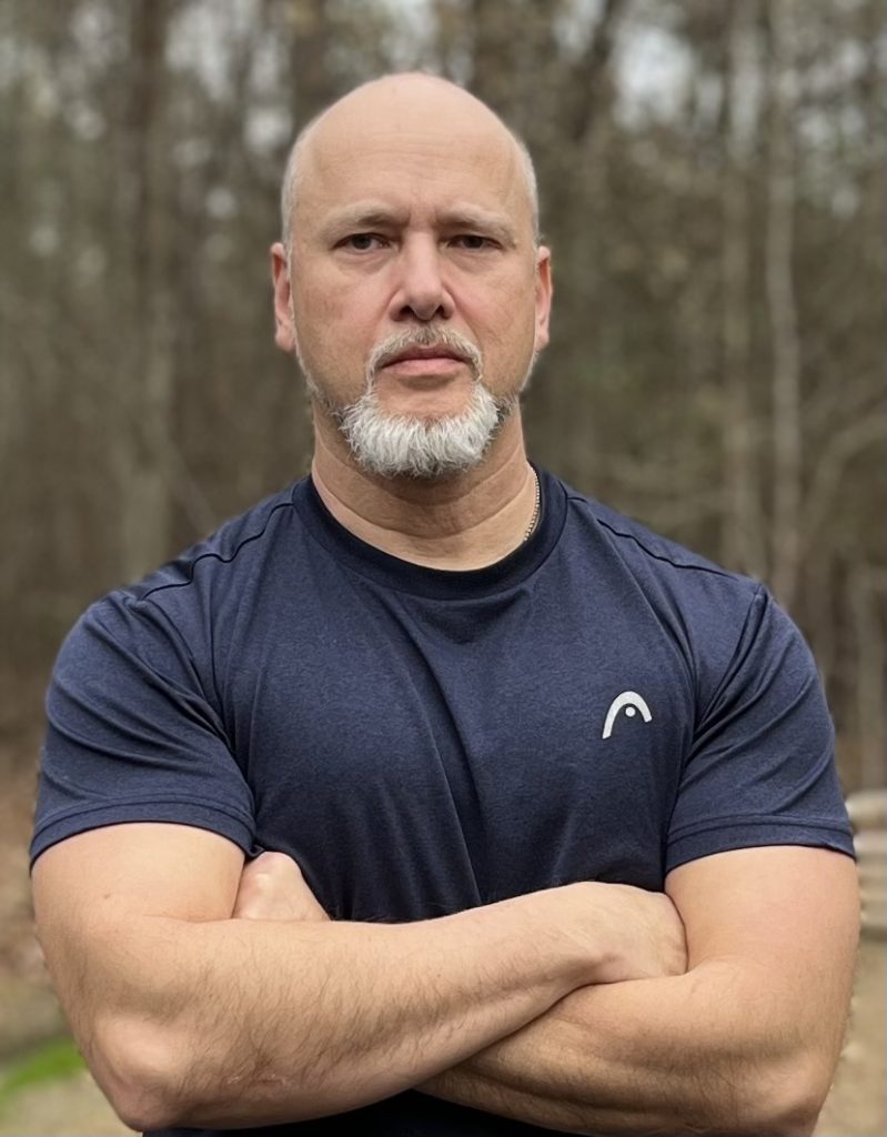 Greg Schreffler, host of The Greg Schreffler Show standing outdoors with arms crossed